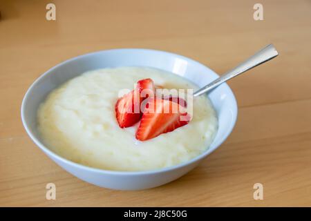 Viele geschnittene Erdbeeren mit Reispudding in einer Schüssel sind fertig zum Essen mit Silberlöffel oder als leckeres Fingerfood und gesunder Snack mit roten Früchten Stockfoto