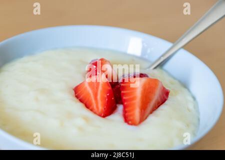 Viele geschnittene Erdbeeren mit Reispudding in einer Schüssel sind fertig zum Essen mit Silberlöffel oder als leckeres Fingerfood und gesunder Snack mit roten Früchten Stockfoto