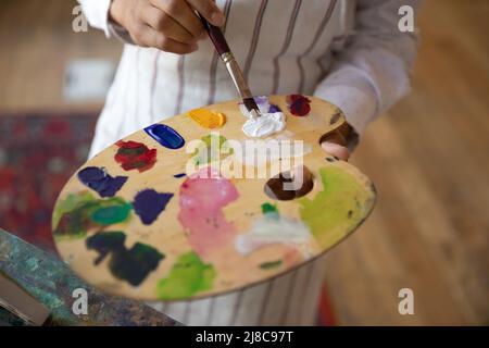 Frau Malerin hält Pinsel mischen Farben auf Holzpalette, Nahaufnahme Stockfoto