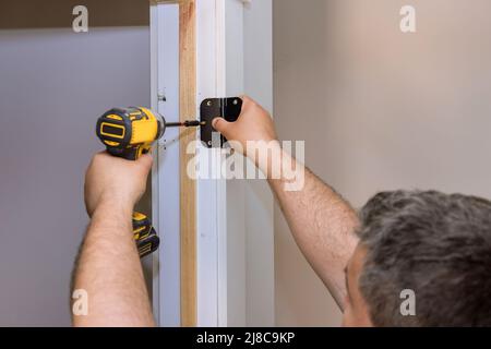 Prozess der Installation Edelstahl Tür Scharniere auf einer weißen Holztür Stockfoto