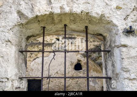 Gewölbtes Fenster mit Metallstangen in altem Mauerwerk. Die Textur des alten verfallenen Mauerwerks. Die alte halb zerstörte Synagoge. Ein Ort für religiöse r Stockfoto