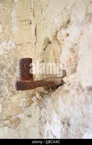 Große antike Schleife in Steinwand eingebettet. Altes Metall mit Rost bedeckt. Die Ruinen einer alten Synagoge. Die Textur des alten verfallenen Mauerwerks. Stockfoto