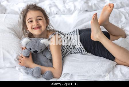 Glückliches kleines Mädchen mit weichem Spielzeug Koala im Bett. Stockfoto