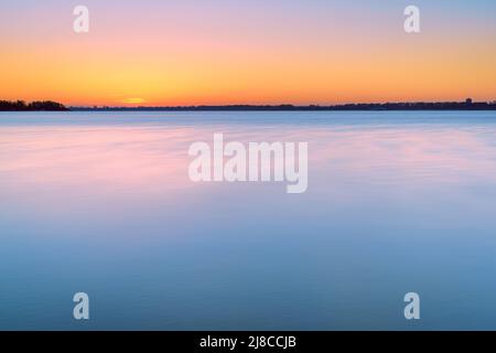 Atemberaubender Sonnenaufgang mit Pastellfarben in Blau und Orange. Langzeitbelichtung Dämmerung am See mit Blick über den niederländischen Veluwezoom am Horizont Stockfoto