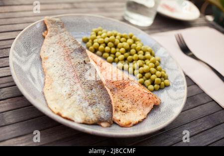 Appetitlich gebackene Forellenfilets mit grünen Erbsen Stockfoto