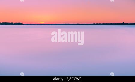Atemberaubender Sonnenaufgang mit Pastellfarben in Blau und Orange. Langzeitbelichtung Dämmerung am See mit Blick über den niederländischen Veluwezoom am Horizont Stockfoto