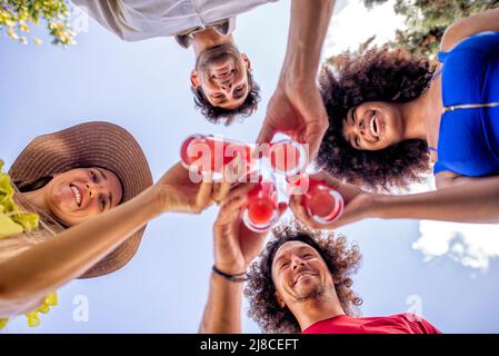 Low-Angle-Ansicht einer multirassischen Gruppe von Freunden genießen einen Drink an heißen Sommertagen. Unter dem Winkel auf glückliche Menschen lächeln vor der Kamera während der Happy Hour. Stockfoto