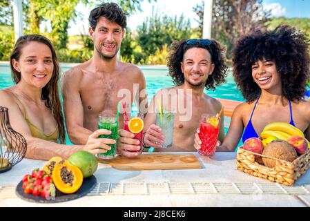 Sommerschwimmbad-Party! Glückliche multirassische Gruppe von Freunden, die im Wasser stehen, mit Getränken, die heiße Feiertage im Freien feiern Stockfoto