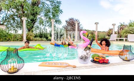 Sommerschwimmbad-Party! Glückliche multirassische Gruppe von Freunden, die sich auf aufblasbarer Matratze mit Getränken entspannen, die heiße Feiertage im Freien feiern Stockfoto