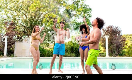 Sommerschwimmbad-Party! Fröhliche, multirassische Gruppe von Freunden, die bei einer Party am Pool mit Weingetränken auf einer Champagner-Dusche tanzen und den Sommer feiern Stockfoto