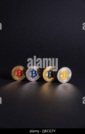 Vier Bitcoin-Münzen mit unterschiedlicher Farbe, ausgerichtet auf schwarzem Hintergrund. BTC Crypto digitale Währungsmünze Internationale Börse. Stockfoto