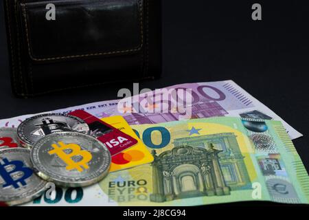 Goldene Bitcoin-Münzen lagen auf Banknoten und Kreditkarten von 100 Euro und 500 Euro. Goldbitcoin auf hundertfünfhundert Euro-Banknoten. Stockfoto