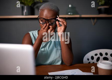 Eine schwarze Geschäftsfrau reibt sich die Augen, während sie spät in der Nacht im Büro arbeitet Stockfoto