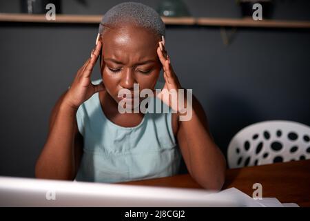 Eine junge schwarze Geschäftsfrau hält ihre Hände am Kopf und arbeitet spät in der Nacht Stockfoto