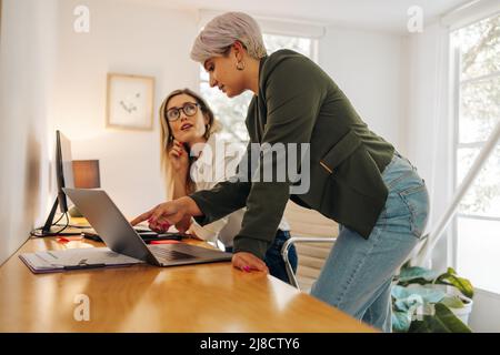 Geschäftsfrau, die in einem modernen Büro mit ihrem Kollegen spricht. Selbstbewusste junge Geschäftsfrau, die bei der Arbeit mit ihrem Kollegen ein Notebook benutzt Stockfoto