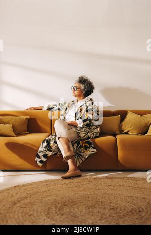 Eine Geschäftsfrau, die auf einer Couch in einer Bürolobby sitzt, schaut nachdenklich weg. Kontemplative Geschäftsfrau, die in einem kreativen Coworkin arbeitet Stockfoto