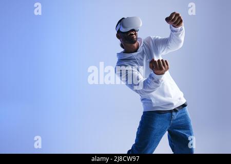 Fröhlicher junger Mann, der in einem immersiven 3D-Videospiel fährt. Glücklicher junger Mann, der lächelt und Spaß hat, während er ein virtuelles Spiel spielt. Mann trägt eine virtuelle r Stockfoto