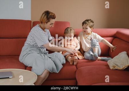 Mutter liest Buch mit zwei Kindern auf dem Sofa. Glückliche Familienmomente zu Hause. Zeit verbringen und Kinder erziehen. Geschwister mit Mama spielen, beobachten Stockfoto