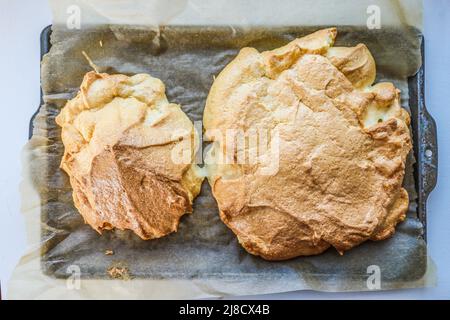 Blick von oben auf zwei Hügel von pavlova oder gekochtes Eiweiß auf gewachsten Papier auf altem Keksblatt. Stockfoto