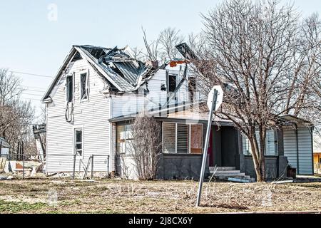 Zweistöckiges Rahmenhaus, das von einem Tornado mit eingehauenen Dacheinstürzungen und Trümmern aus dem Fenster im zweiten Stock im ländlichen Oklahoma USA getroffen wurde Stockfoto