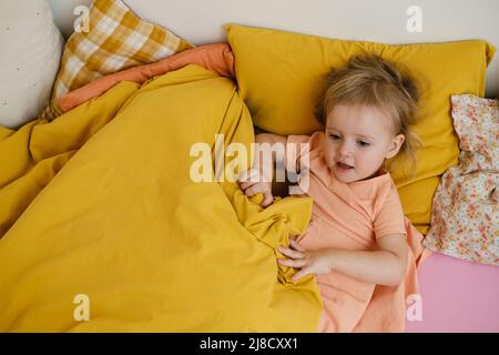 Kinder, die am Morgen auf dem bunten Bett spielen, können sich verstecken. Glückliches Kind liegt auf rosa Bett. Schwester und Bruder im Schlafzimmer, Draufsicht, Kopierraum. Kleinkind Stockfoto