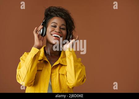 Porträt einer glücklichen jungen Frau, die in Kopfhörern Radio hört und die Kamera anlächelt Stockfoto