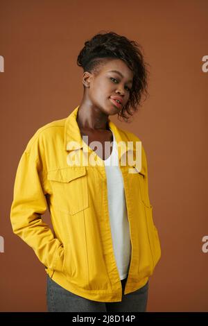Porträt einer selbstbewussten jungen schwarzen Frau in einer Jeansjacke in Gelb beim Blick auf die Kamera Stockfoto