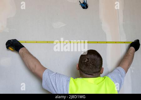 Der Assistent misst den Abstand an der Wand mit einem Maßband Stockfoto