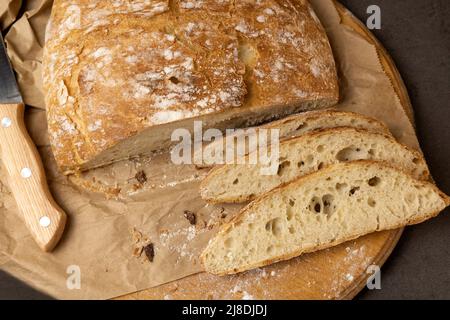 Weiße Brotscheiben und Messer. Ein Laib Brot mit der ersten Hälfte bereits geschnitten. Drei Scheiben Brotscheiben. Blick von oben. Stockfoto