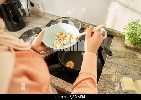 Beschnittenes Foto einer jungen Frau, die in der Küche Käsepfannkuchen mit Rosinen kocht Stockfoto