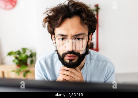 Der junge bärtige Mann mit Brille arbeitete von zu Hause aus konzentriert auf den Laptop Stockfoto