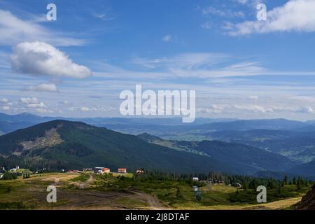 Gemütliches Dorf in den Bergen, mit ländlicher Straße auf Hochland Feld. Luftaufnahme der Bergsiedlung, mit kleinen Häusern und Gebäuden im Sommer, mit Berglandschaft im Hintergrund. Konzept von Hochland. Stockfoto