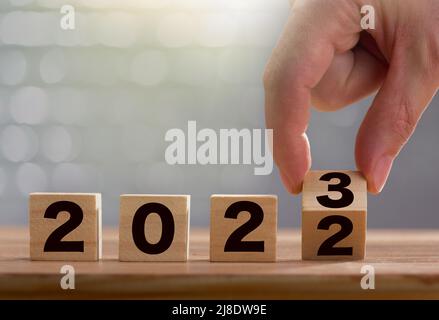 Der Mann dreht den Block 3 mit den Fingern. Holzblöcke mit 2022 - 2023 Nummer auf dem Tisch. 2023 Neujahrs-Konzept Stockfoto