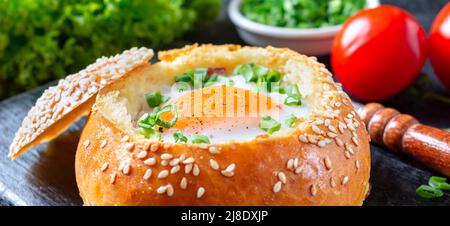 In einem Brötchen gebackene Eier mit Schinken, Käse und grünen Zwiebeln, Nahaufnahme. Banner, schwarzer Hintergrund Stockfoto