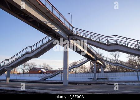 Es gibt eine Fußgängerbrücke über die Eisenbahnschienen. Eine Brückentreppe verbindet eine Plattform mit einer anderen am Bahnhof Stockfoto