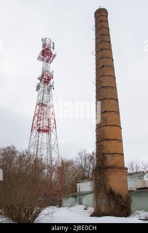 Alt und neu. Ein Zellenturm auf dem Hintergrund eines Ziegelkamins eines alten Kesselhauses. Stockfoto