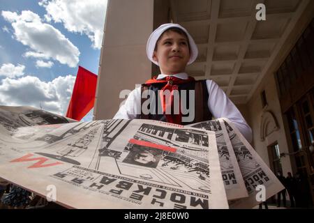 Moskau, Russland. 15.. Mai 2022. Ein Junge, der als Pionier der 1930 gekleidet ist, verteilt die Ausgabe der Zeitung Vechernaya Moskva vom 14. Mai 1935 mit Informationen über die Eröffnung der U-Bahn in Moskau. Park Kultury Station reenacts, an einer Straße vor einem Eingang zum Bahnhof, die Zeremonie 1935 zum Start der ersten Linie überhaupt, um den 87.. Geburtstag der Moskauer Metro, Russland zu feiern Stockfoto