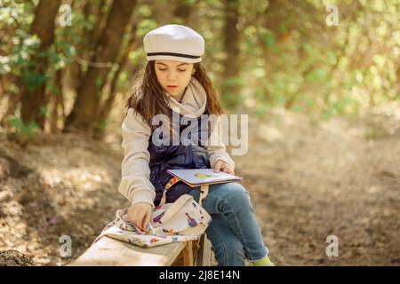 Kleines Mädchen malt im Frühling im Freien blühenden Märchenpark. Kinderzeichnungen. Kreatives Kind. Freude an der Kindheit. Hochwertige Fotos Stockfoto