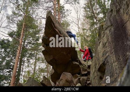Weibliche Wandererin, die dem Mann hilft, von der Klippe herunter zu klettern Stockfoto