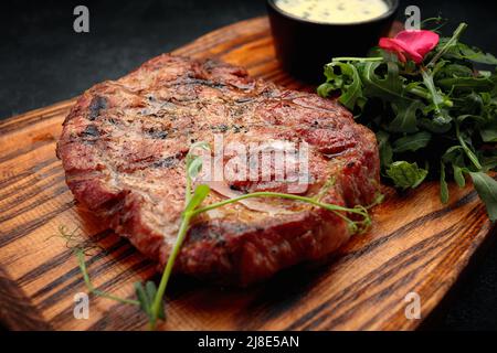 Schweinehals-Steak mit Sauce und Rucola, auf einem Holzbrett Stockfoto