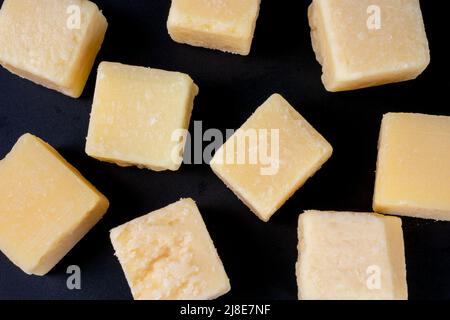 Parmesan-Käsewürfel auf schwarzem Hintergrund. Grana padano Hartkäsestücke Draufsicht Stockfoto