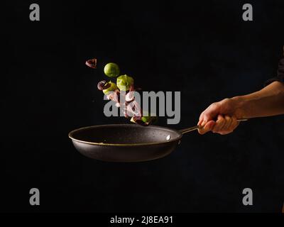 Der Koch kocht kleine Oktopusse mit Gemüse in einer Bratpfanne. Levitation. Essen auf schwarzem Hintergrund. Das Konzept ist Rezepte zum Kochen vegetarisch Stockfoto