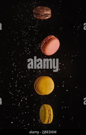 Zwei Makronen - gelb und rosa auf schwarzem Hintergrund mit weißen Zuckerkörnern in einem gefrorenen Flug. Französisches Gebäck, Süßigkeiten, Patisserie, Supermarkt, ca. Stockfoto