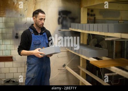 Der Arbeiter stellt die Schachtel auf das Regal. Mann faltet bemalte Bretter. Guy arbeitet in der Holzwerkstatt. Stockfoto