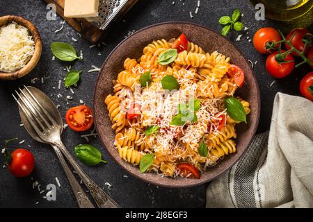 Italienische Pasta alla arrabiata mit Basilikum und Parmesan auf einem Tisch aus dunklem Stein. Stockfoto