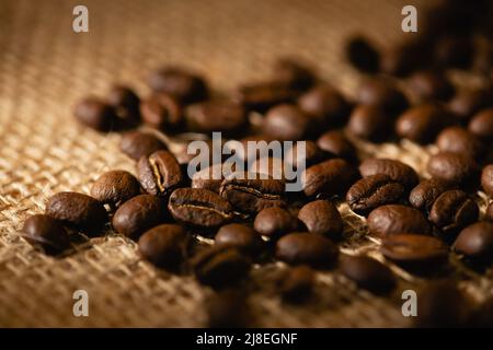 Nahaufnahme einer Streuung von Kaffeebohnen auf einem dunklen Sackleinen-Hintergrund. Stockfoto