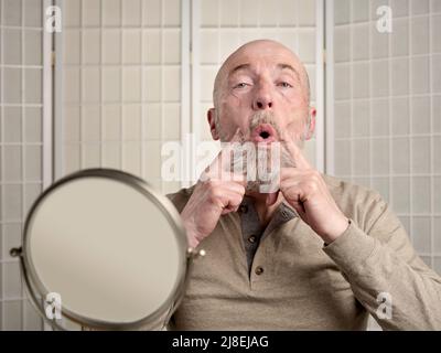 Kopf- und Schulterporträt eines kahlen, bärtigen älteren Mannes, der eine Gesichtsstraffung (Eye Toner) durchführt, und ein Selbstpflegekonzept Stockfoto