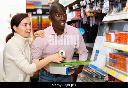 Junges Paar zeigt während des Einkaufens auf Regale mit Bürobedarf im Schreibwarenladen Stockfoto