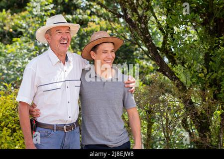 Vater und Sohn verbringen Zeit miteinander und kuscheln Seite an Seite, während sie miteinander lachen. Vater und Sohn lateinische Landarbeiter tragen Hüte zusammen auf einem heißen Stockfoto