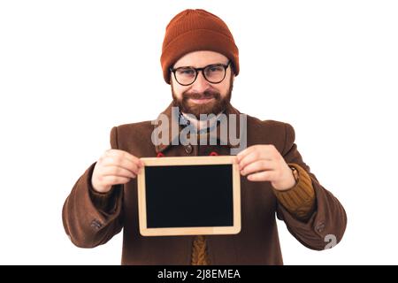Attraktiver hübscher Hipster-Typ, der in warmer Winter- oder Herbstkleidung gekleidet ist und die Kamera mit einer winzigen hölzernen Kopie-Tafel anschaut. Hochwertige Fotos Stockfoto